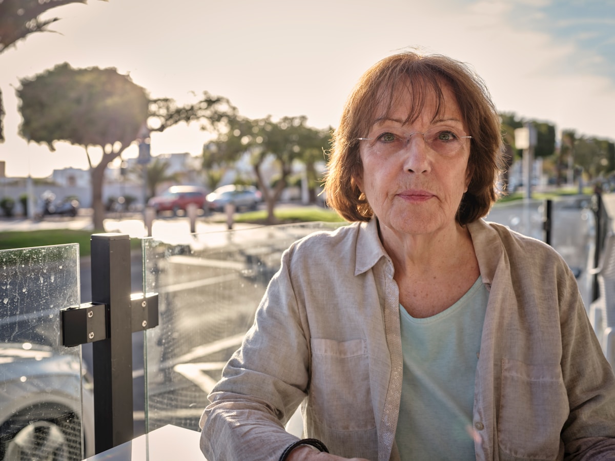 Femme âgée aux cheveux bruns, debout dans un environnement urbain.