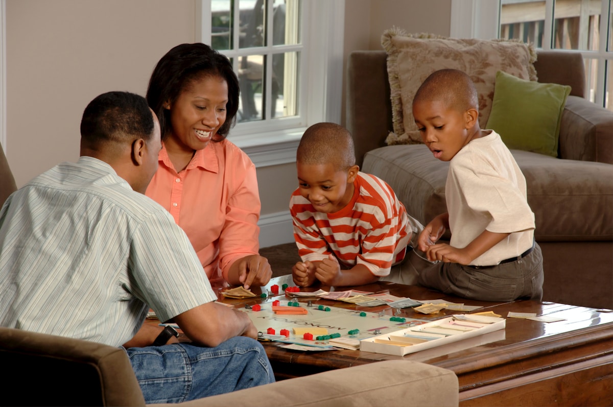 Famille afro-américaine jouant à un jeu de société ensemble dans un salon confortable.