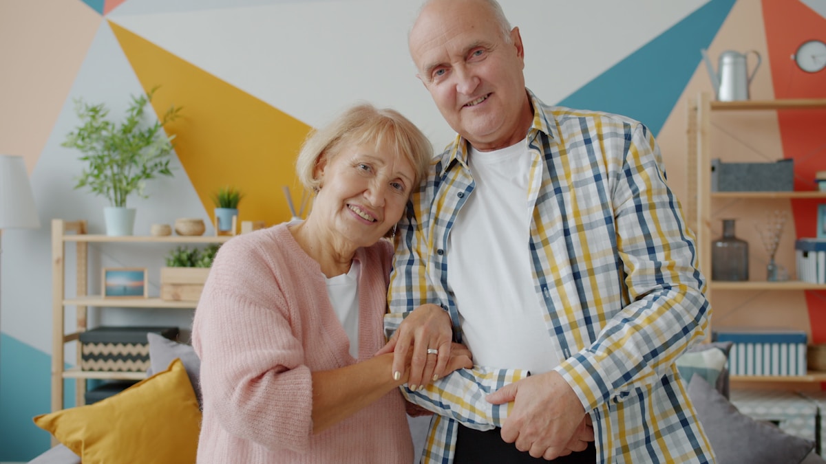 Un couple âgé souriant dans un intérieur coloré et accueillant.