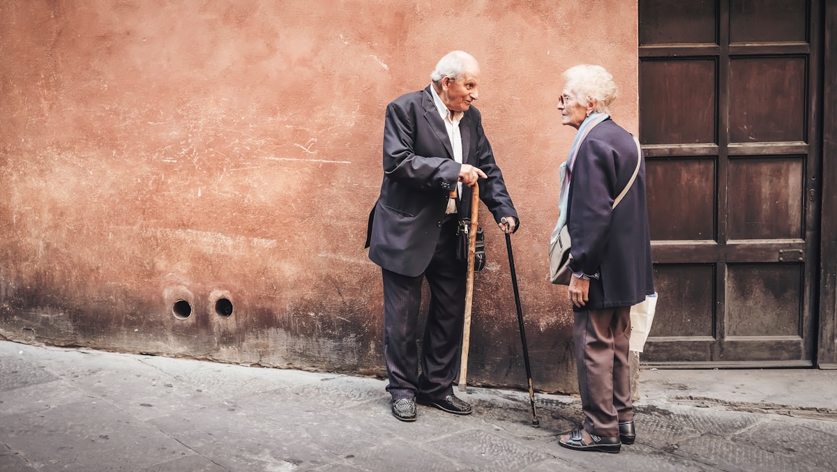 Deux hommes âgés en conversation, appuyés contre un mur.