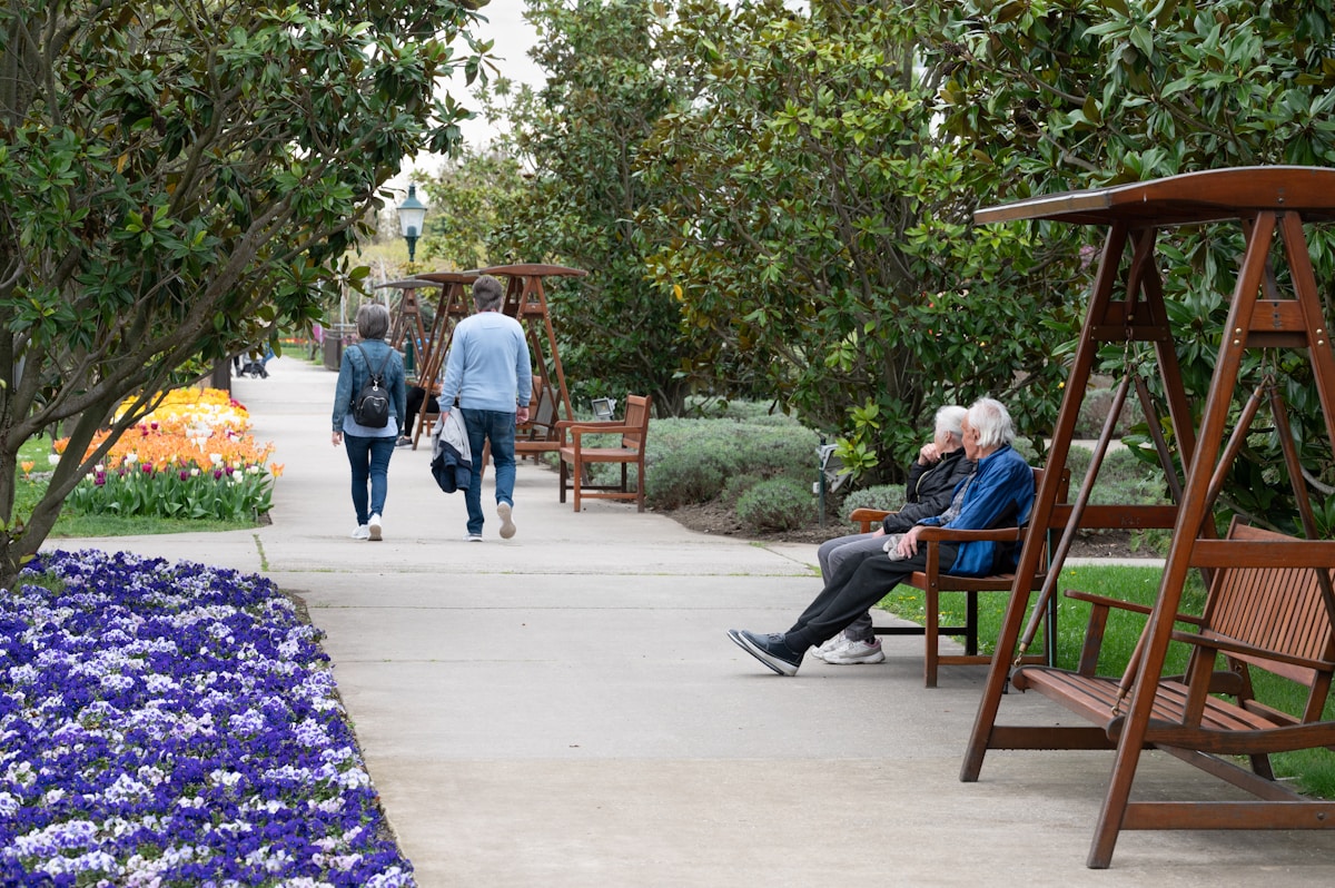 Allée de jardin avec bancs, fleurs colorées et promeneurs.