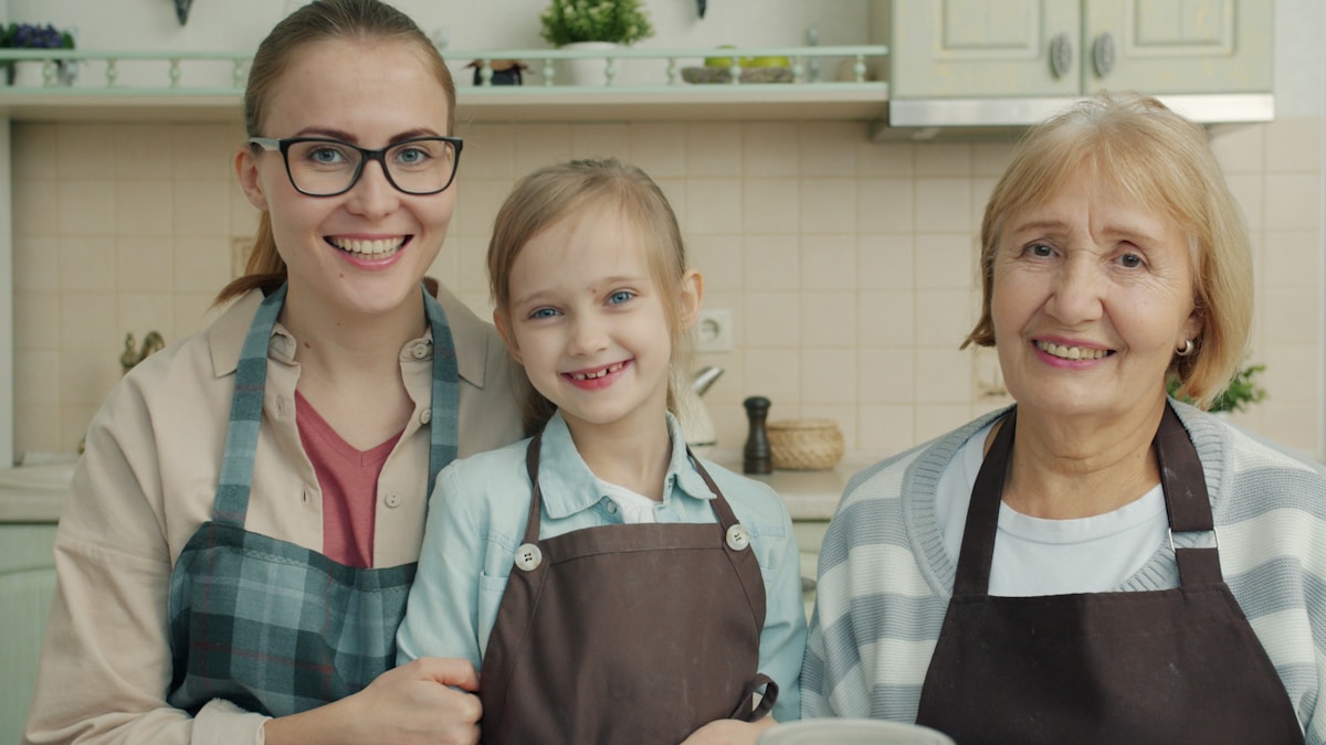 Trois générations de femmes souriantes dans une cuisine familiale.