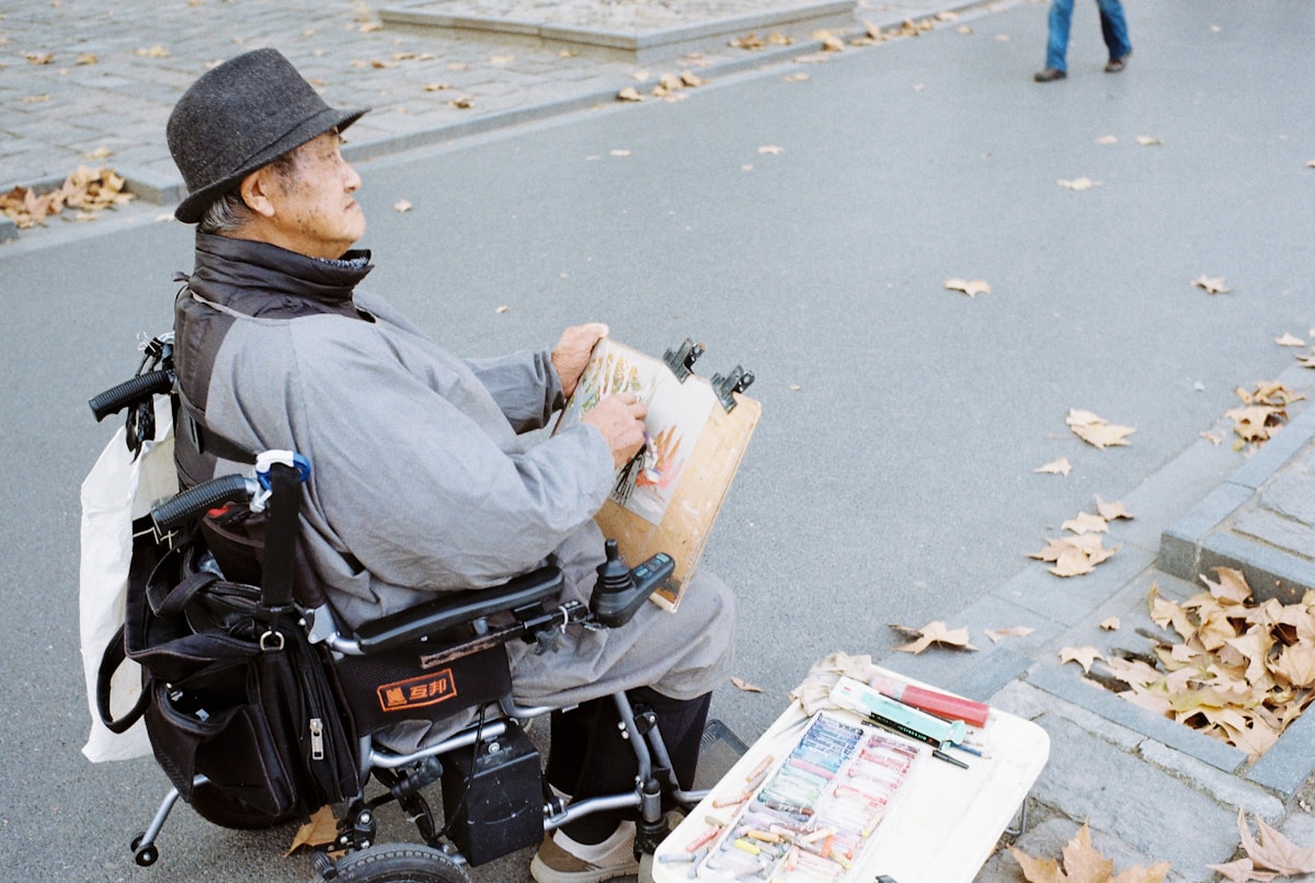 Homme en fauteuil roulant peignant sur un chevalet dans la rue.