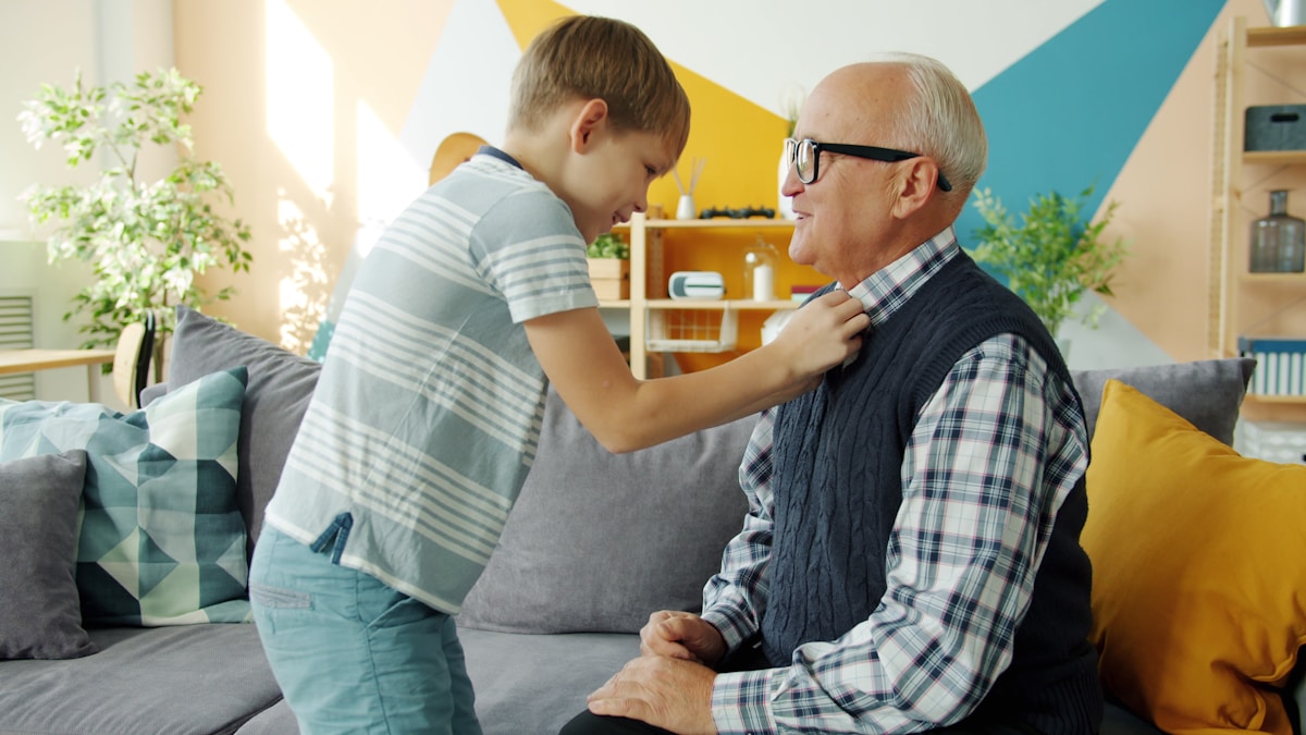 Un jeune garçon ajuste la cravate de son grand-père dans un salon coloré.