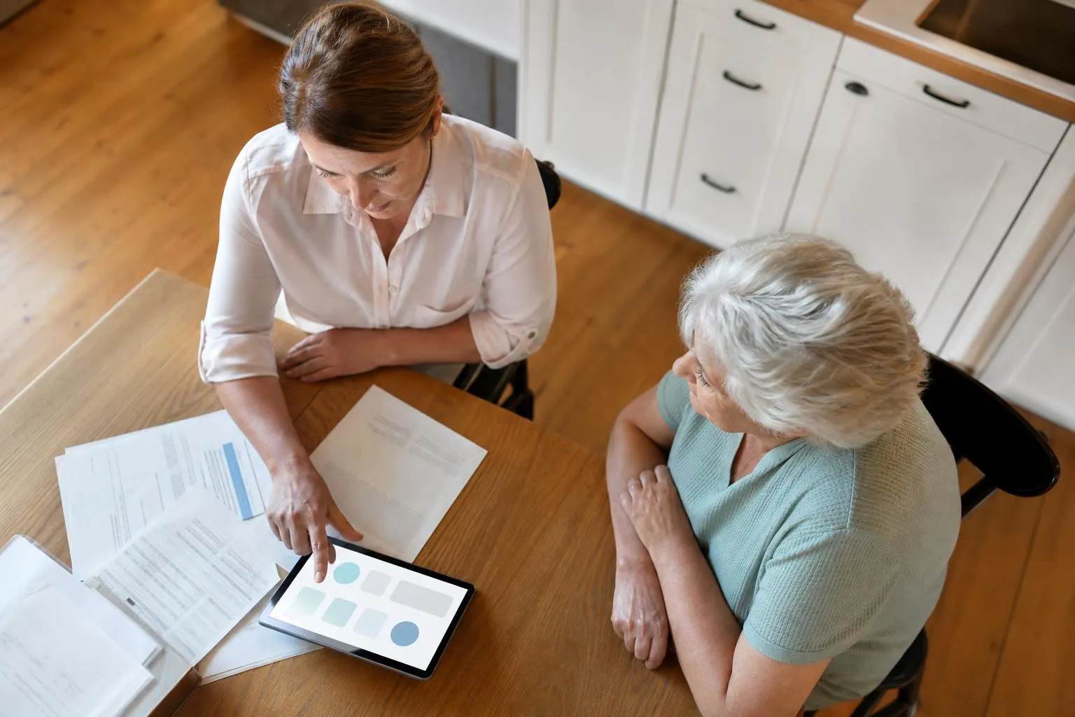 Femme d'affaires discutant avec une femme âgée sur des documents et une tablette.
