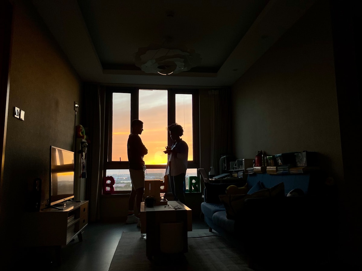 Deux personnes debout dans une pièce sombre, observant le coucher de soleil.