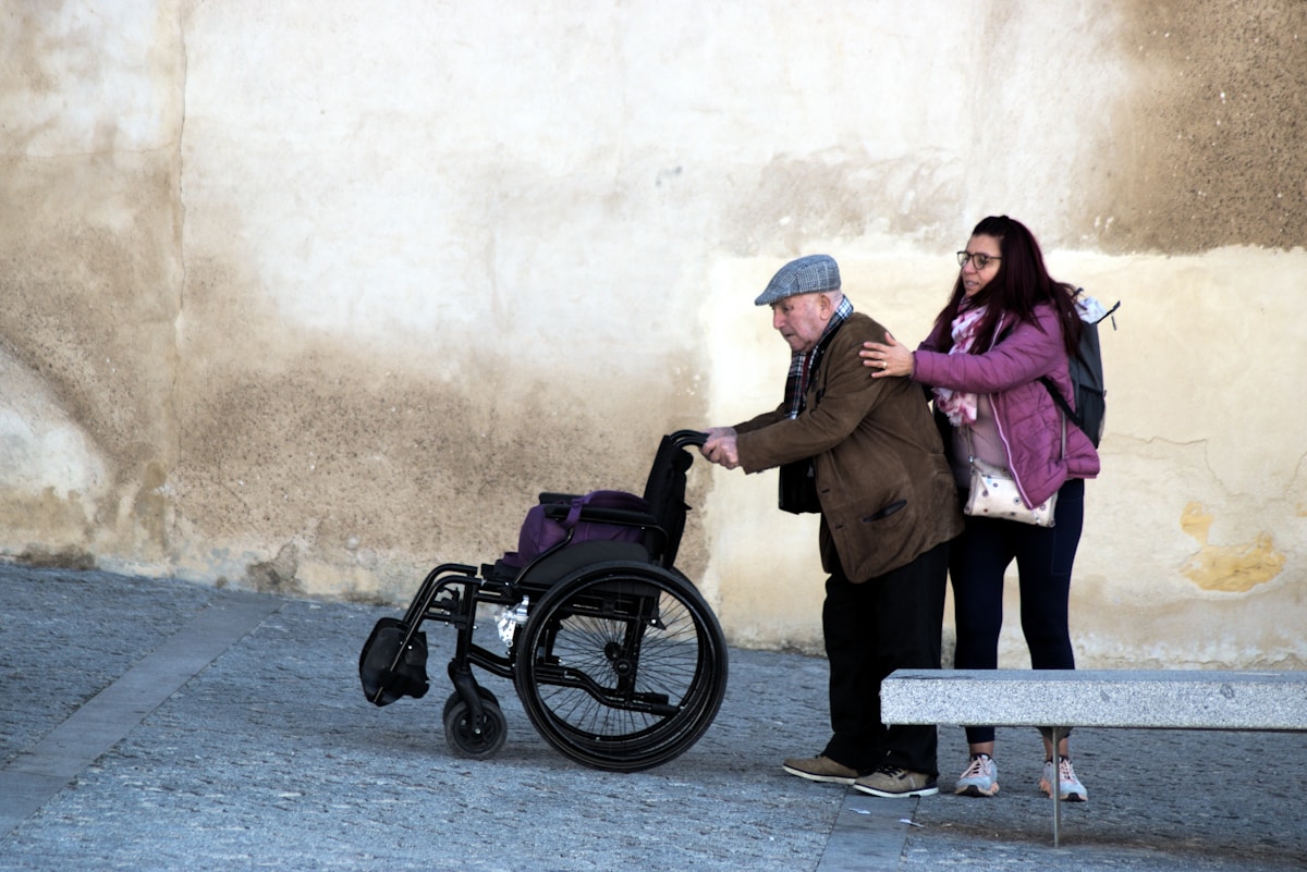 Homme âgé en fauteuil roulant aidé par une femme.