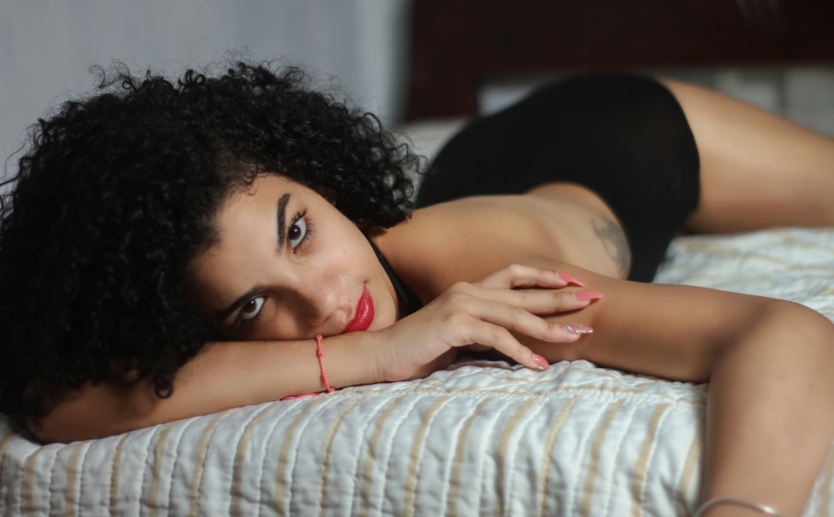 Femme aux cheveux bouclés, lèvres rouges, allongée sur un lit.