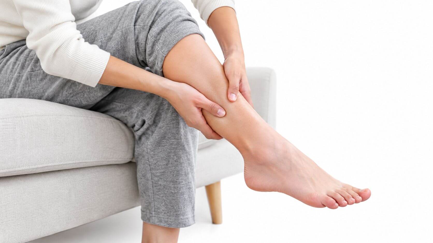 A person sitting on a couch gently massages his calf to relieve pain in the leg.
